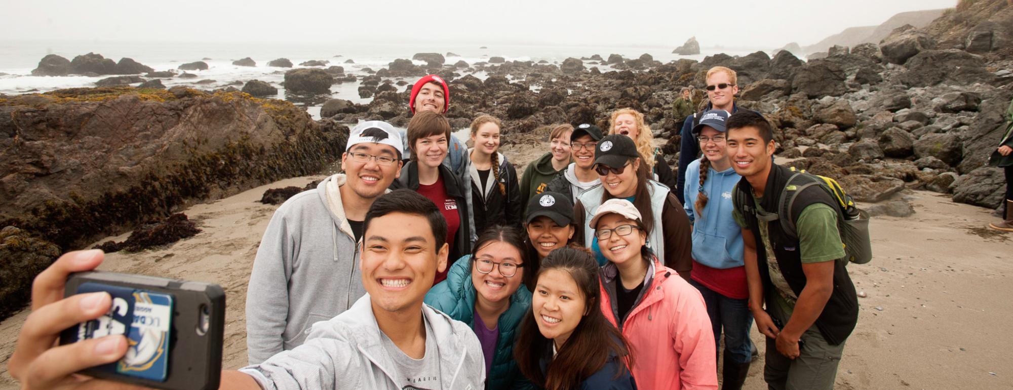 A group of students taking a selfie on a coastal beach.