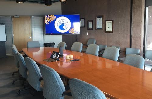 A large conference table lined with chairs. In the corner is a TV with the BML logo displayed.