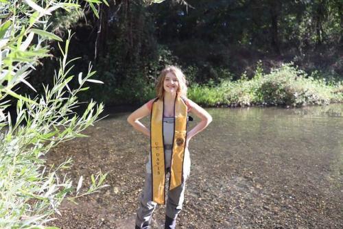 A person in wading gear and a UC Davis graduation stole