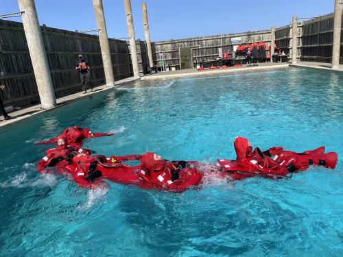 Several people in red survival suits floating in formation in a pool