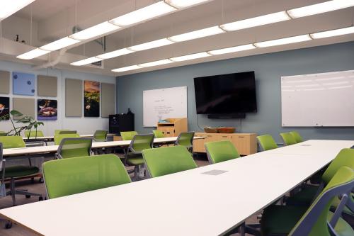 A large conference room with tv screen, two whiteboards on the wall, and several tables and chairs.