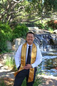 A man standing in front of an outdoor background with a UC Davis graduation stole